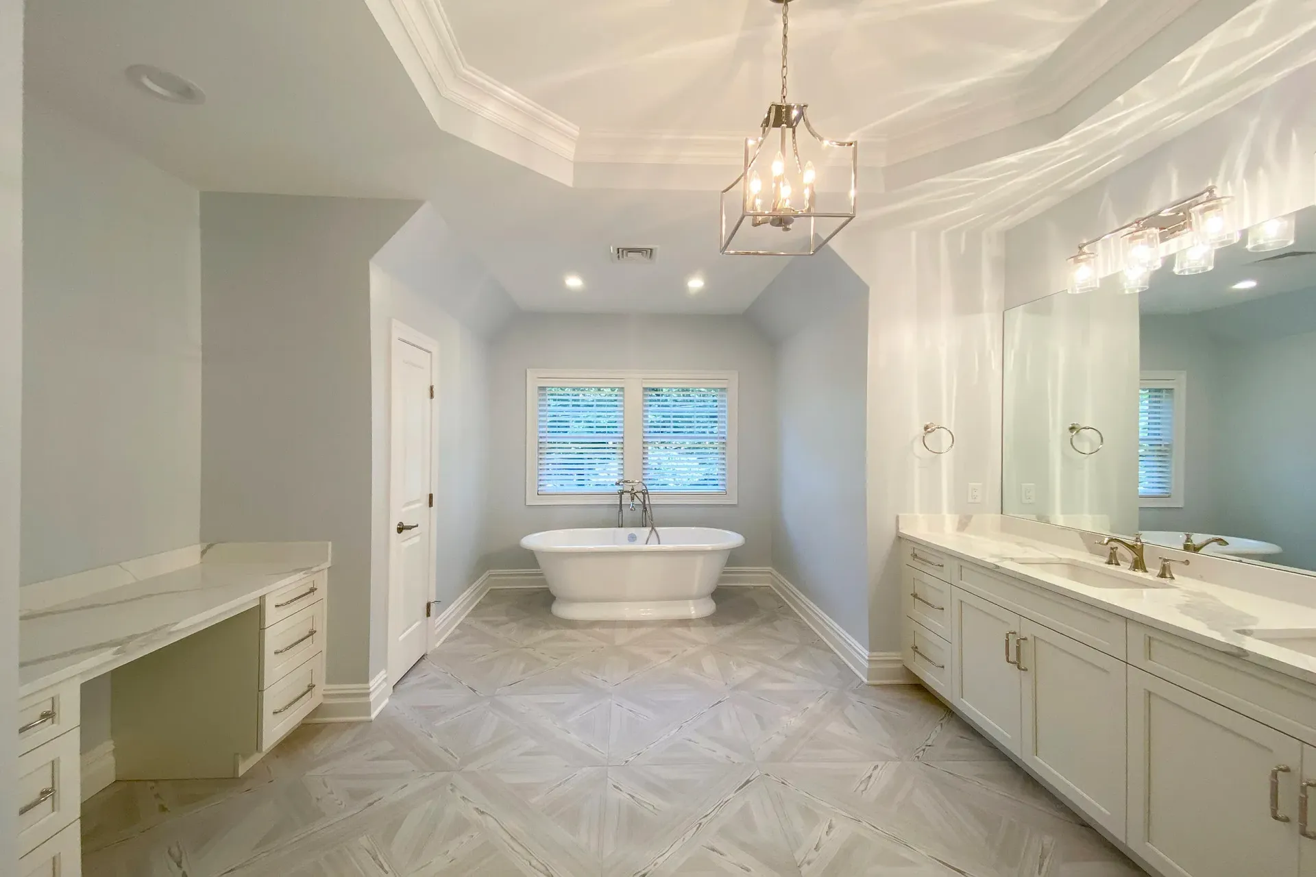 Spacious, light-blue bathroom with a free-standing tub, double vanity, and a window with blinds.