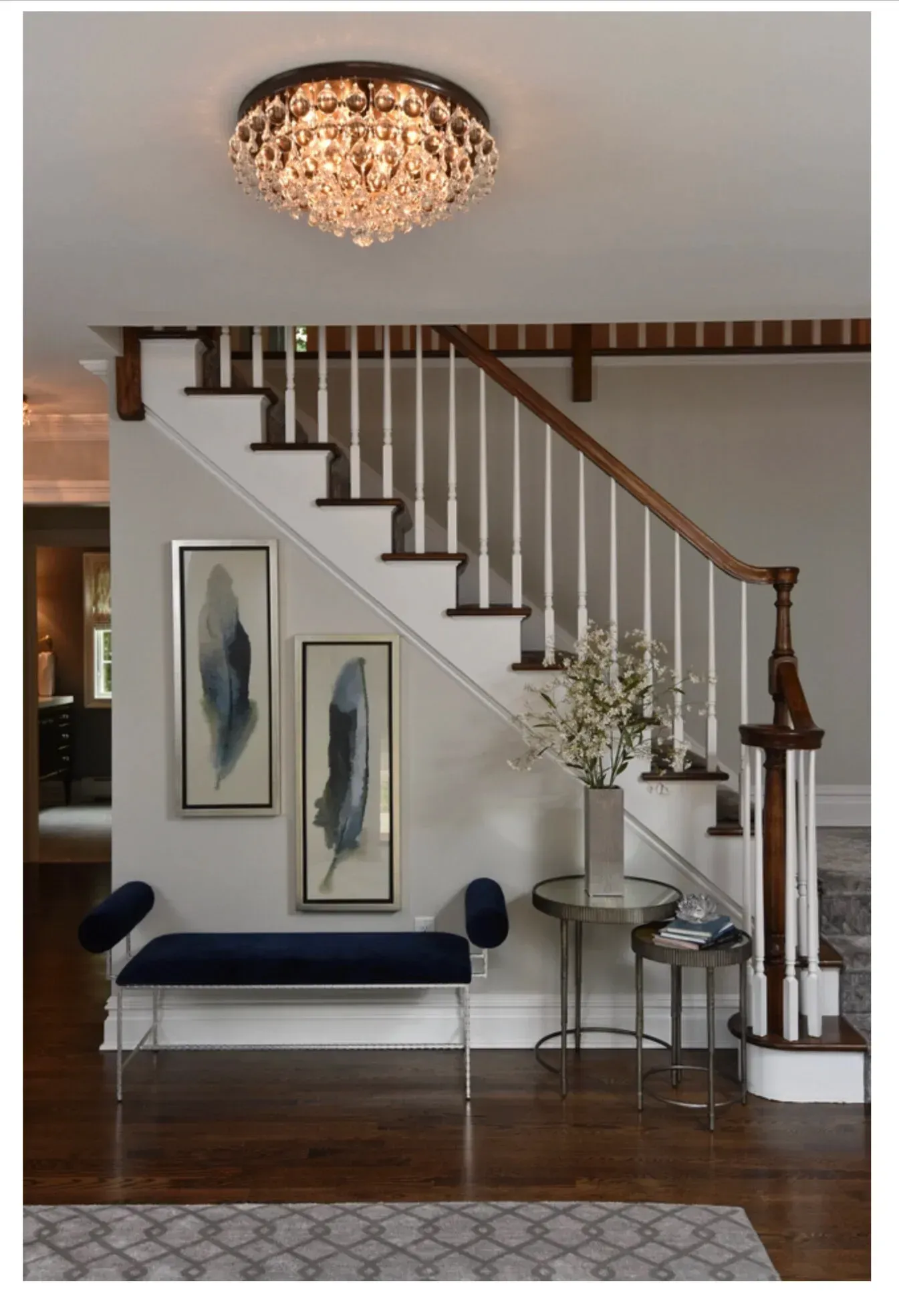 Staircase with white steps, wooden handrail, blue bench, artwork, and crystal chandelier.