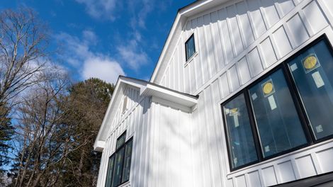 White farmhouse exterior with black-framed windows against a blue sky.