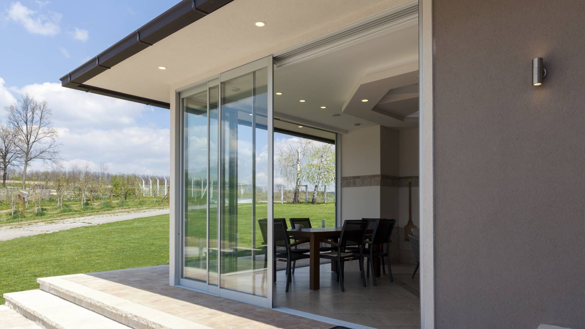 Sliding glass doors open to a dining area with a table and chairs; a patio, grass, and trees are outside.