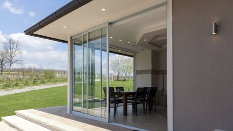 Sliding glass doors open to a dining area with a table and chairs; a patio, grass, and trees are outside.