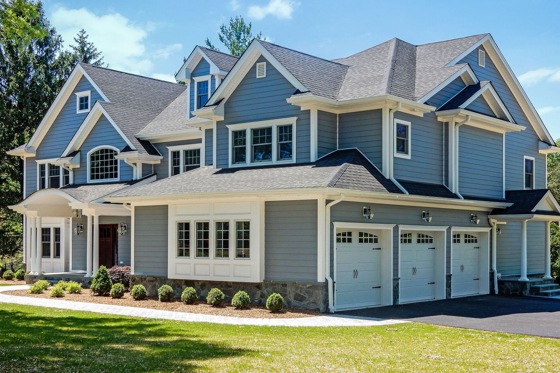 Blue and gray two-story house with a three-car garage and manicured lawn.