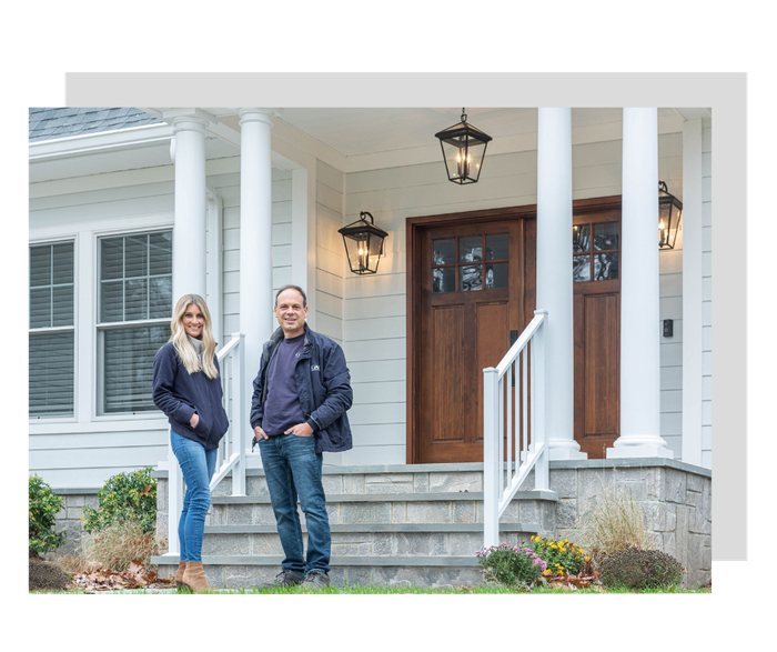 Couple stands on steps of home with wooden door and lanterns.