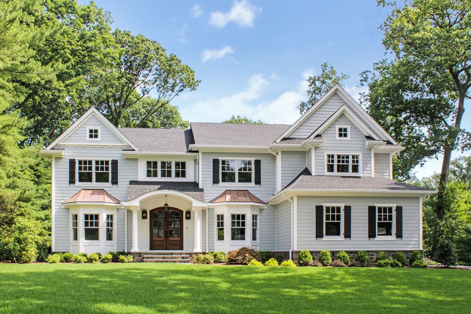 Gray two-story house with black shutters, copper accents, and a green lawn.