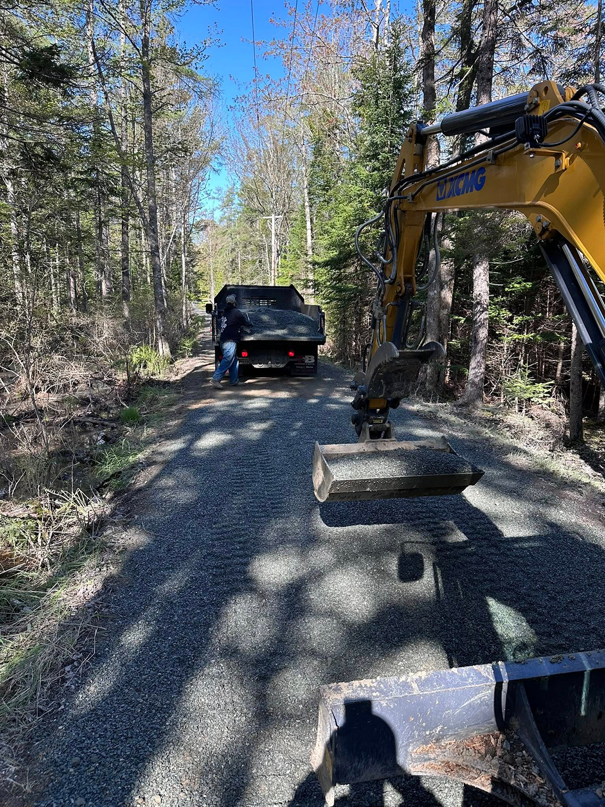 Gravel road with a truck and excavator; trees on either side. Sunny day.