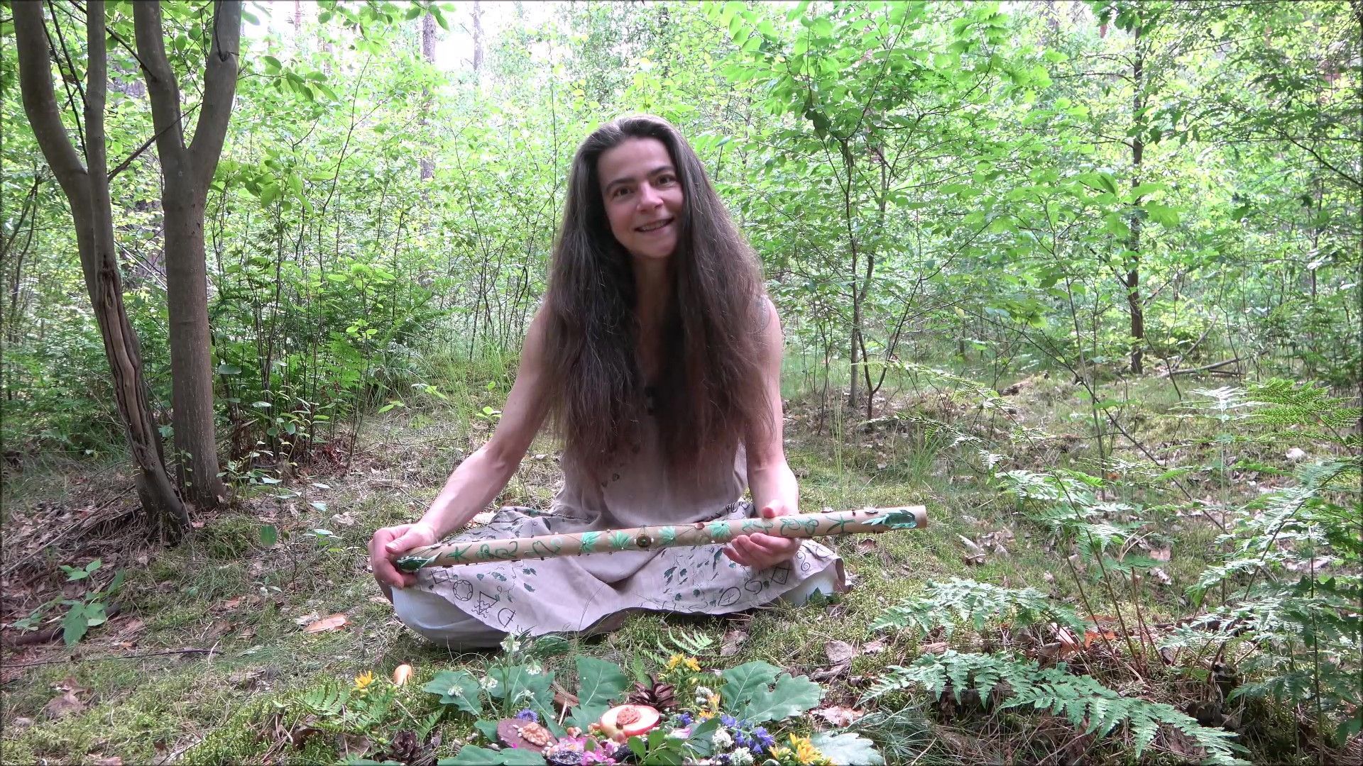 Eine Frau sitz im Wald auf dem Boden und hält eine Bambusflöte