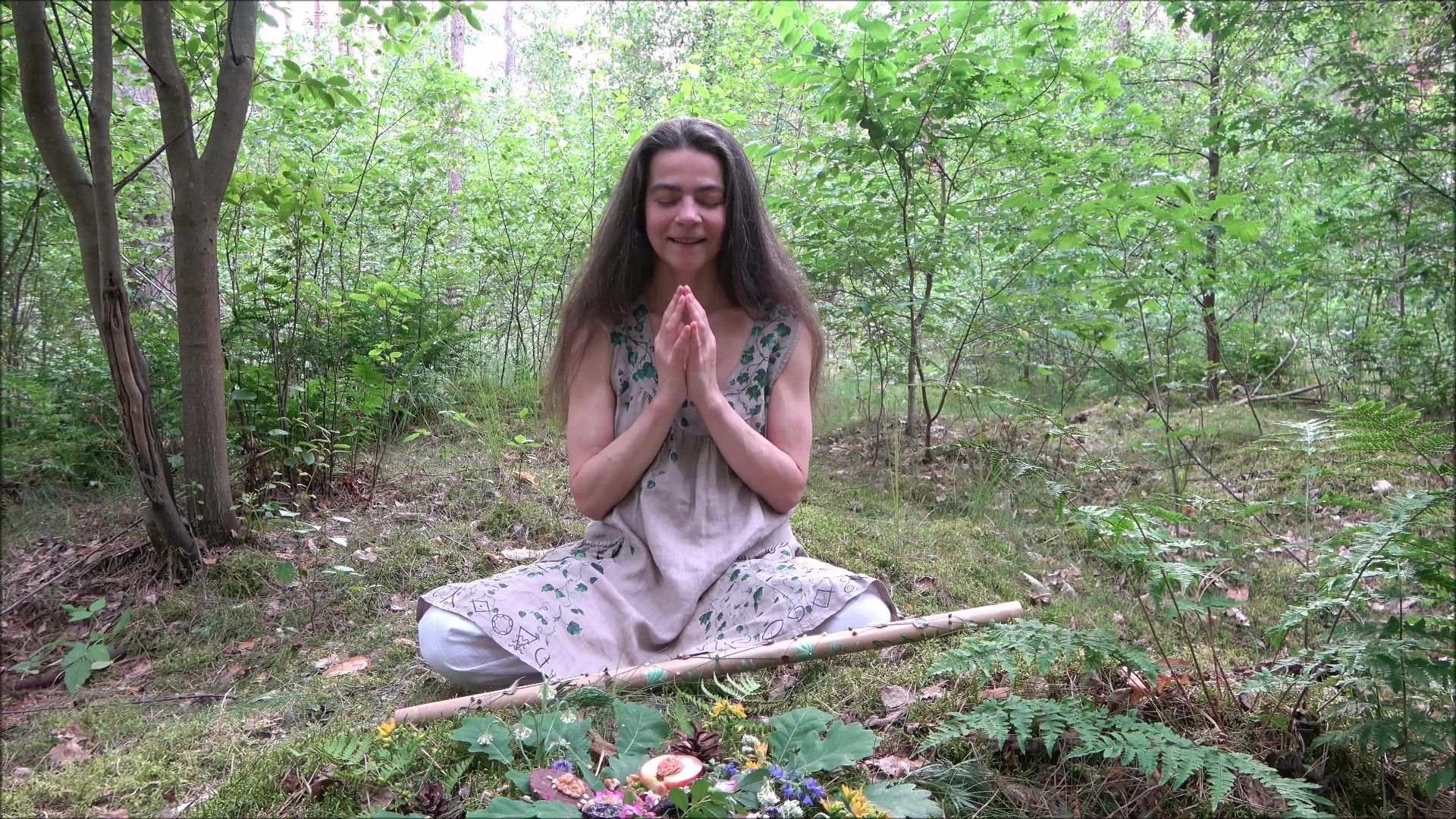 A woman is sitting in a lotus position in the woods with her hands folded.