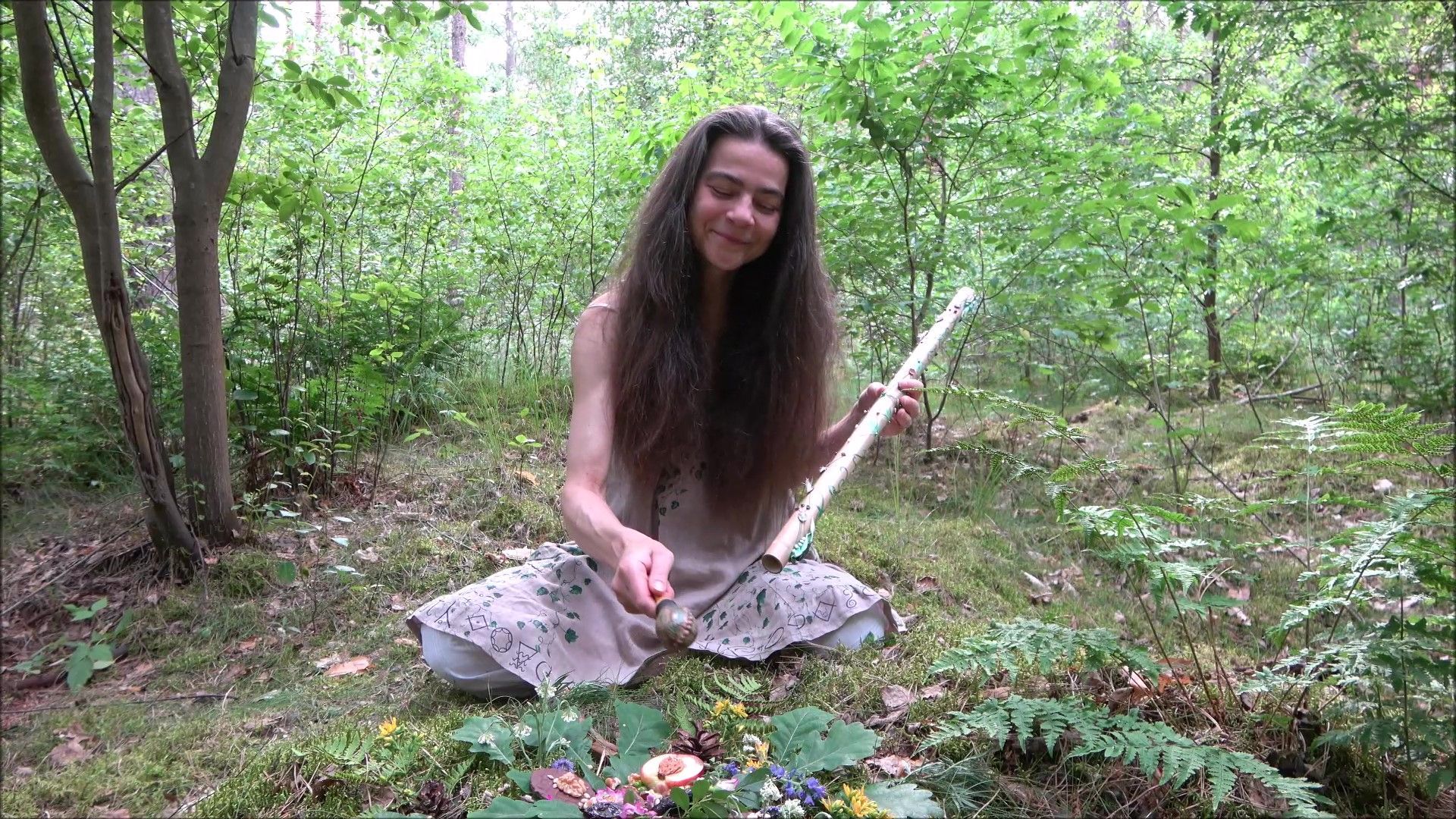 Eine Frau sitzt auf dem Boden im Wald und hält eine Flöte und Rassel