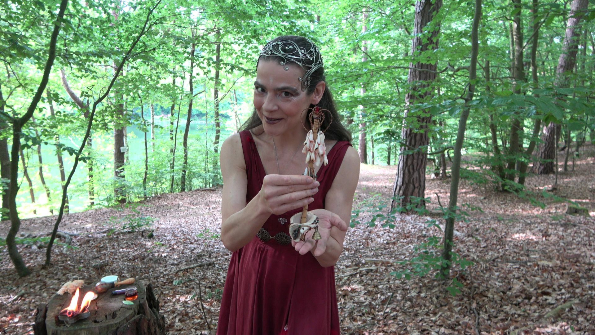 Eine Feuerfee im roten Kleid hält im Wald ein Zepter in der Hand