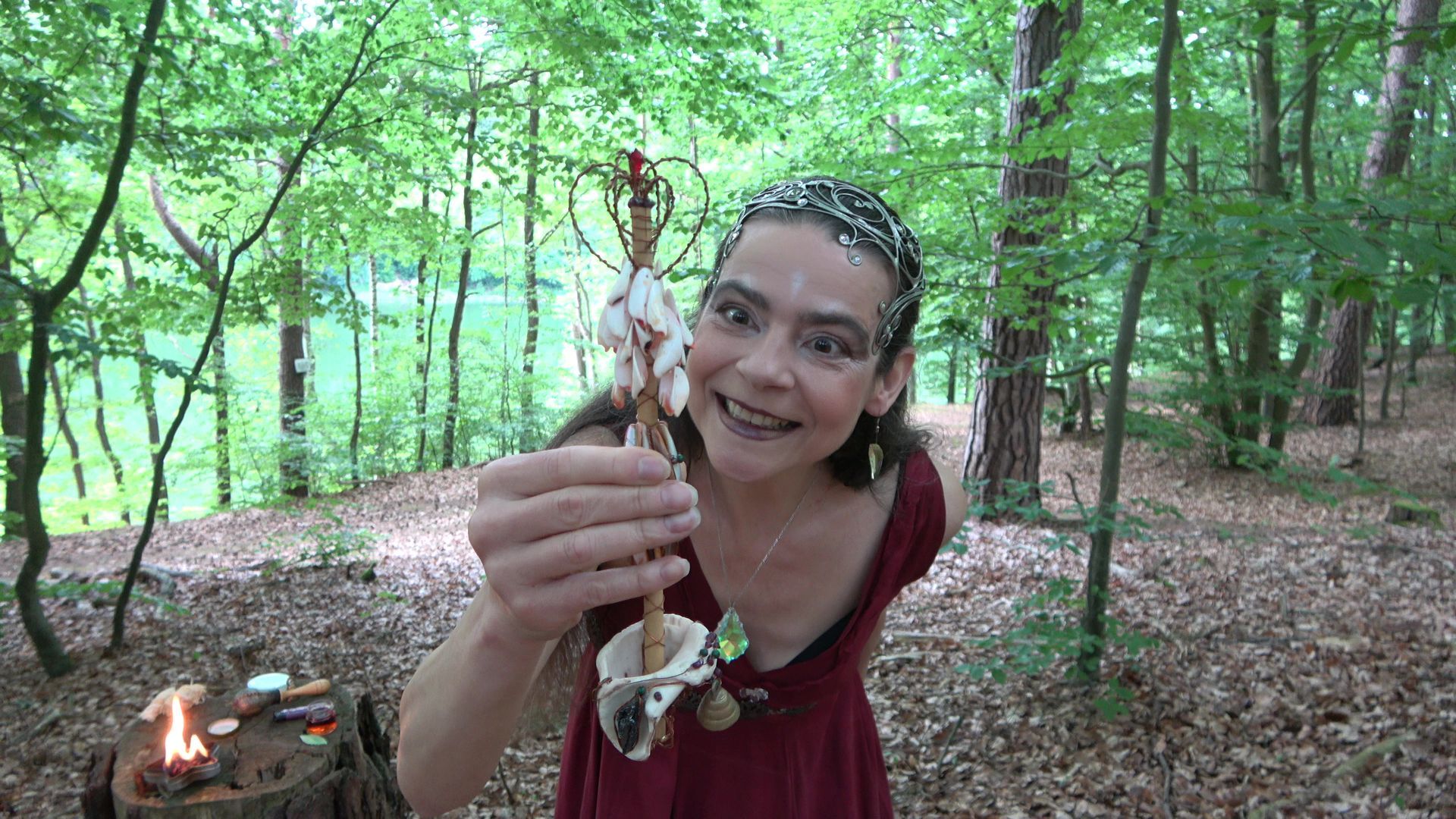 Eine Feuerfee im roten Kleid hält im Wald ein Zepter in der Hand