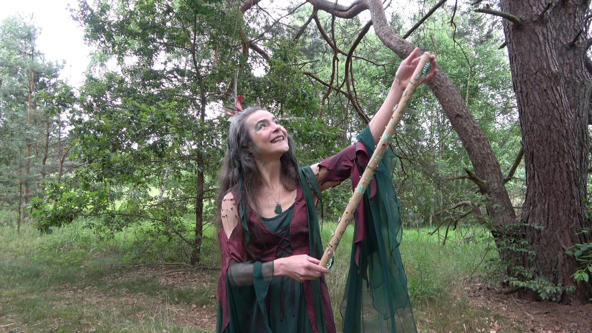 Eine Frau im grünen Feenkleid hält eine Flöte im Wald