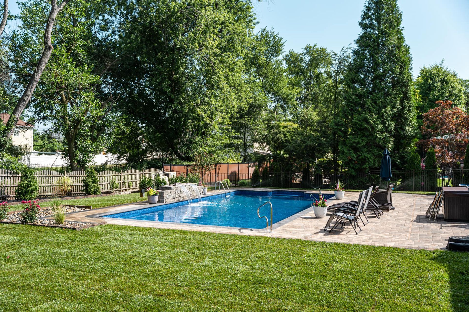 There is a large swimming pool in the backyard surrounded by trees.