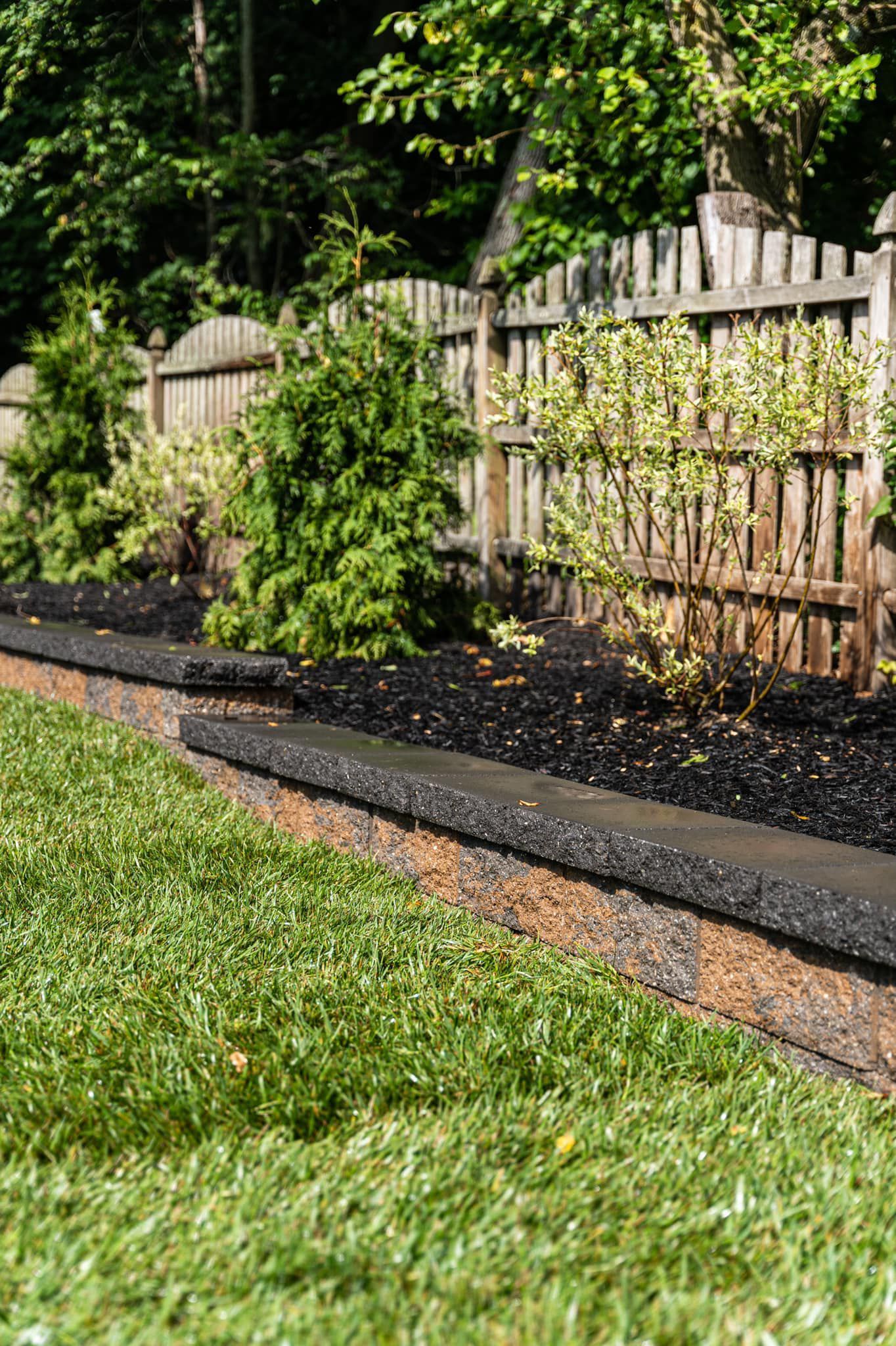 A wooden fence surrounds a lush green lawn in a backyard.