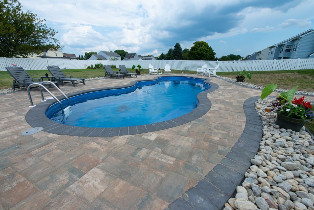 A large swimming pool is surrounded by chairs and rocks in a backyard.