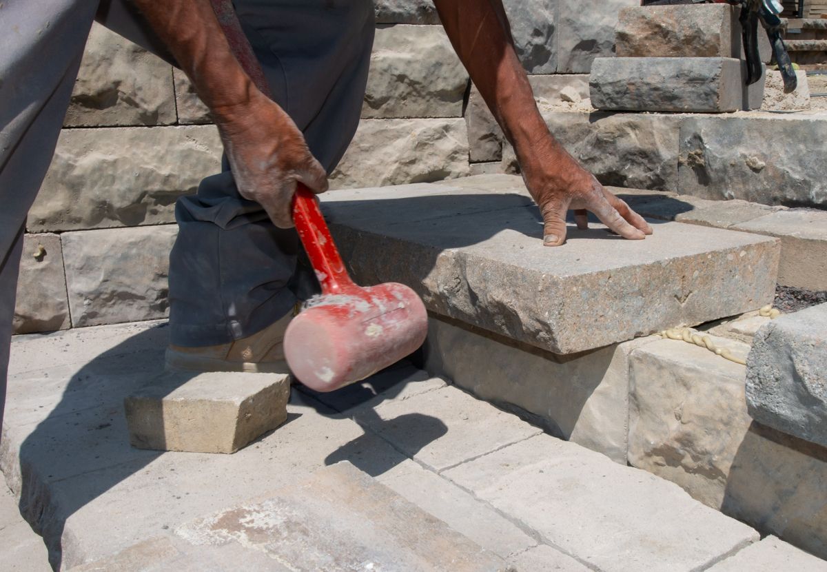 A man is using a red hammer to break bricks
