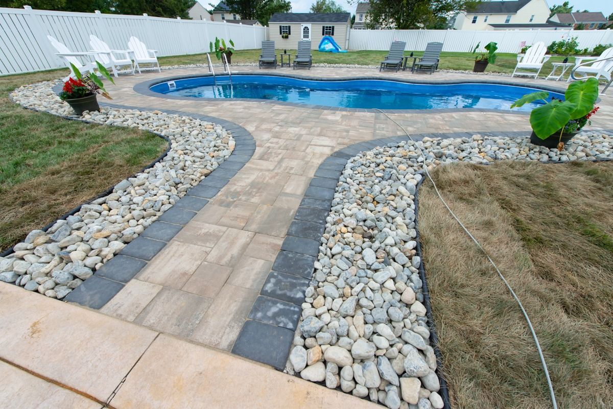 A large swimming pool surrounded by rocks and lawn chairs in a backyard.