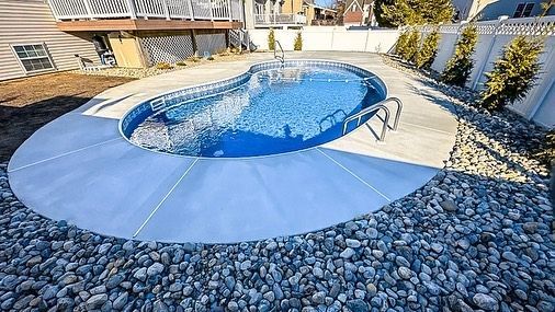 A large swimming pool is surrounded by rocks in a backyard.