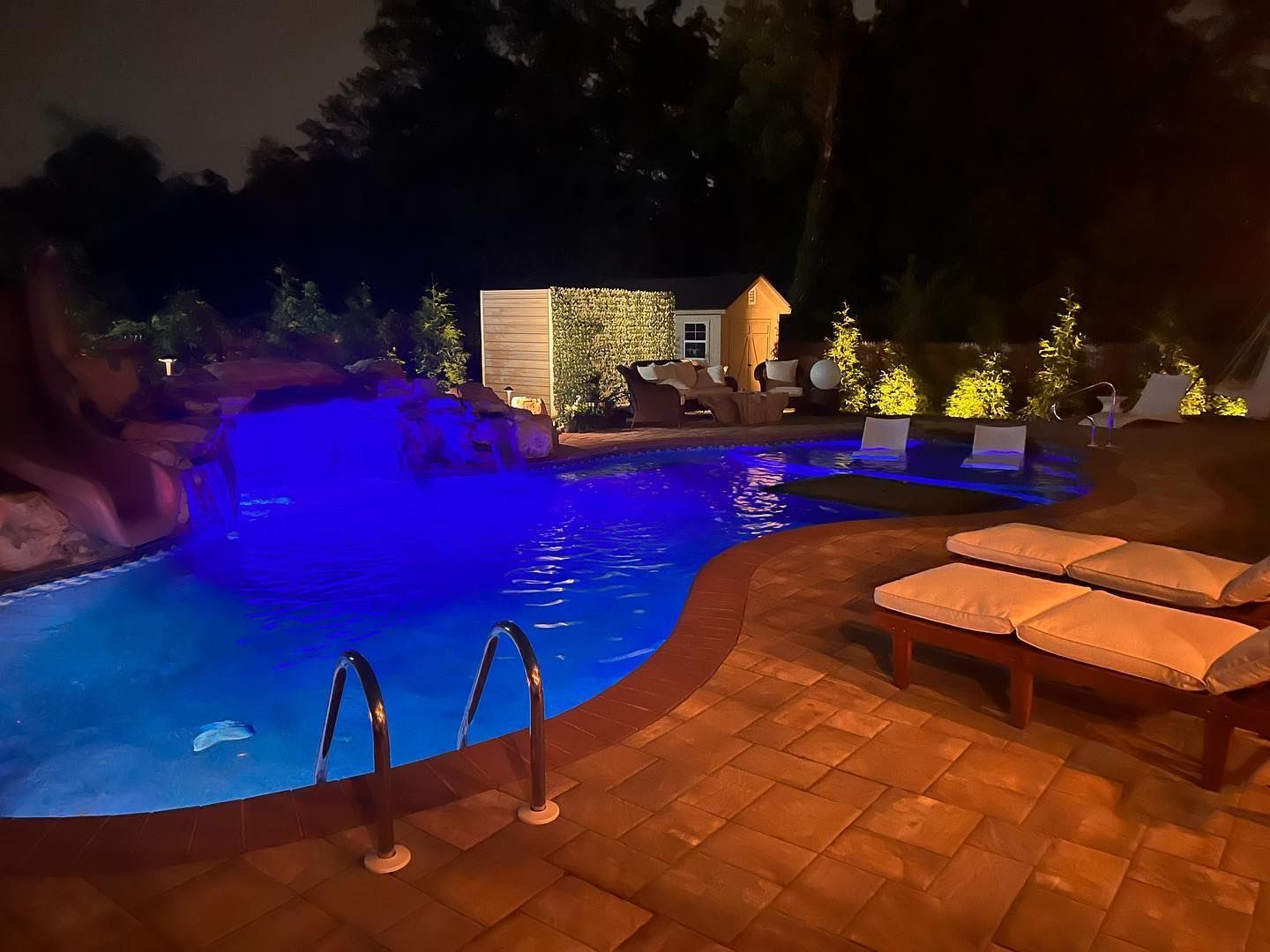 A large swimming pool is lit up at night with blue lights.