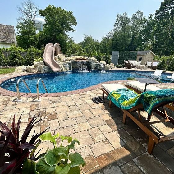 A large swimming pool with a slide and a waterfall in the backyard.