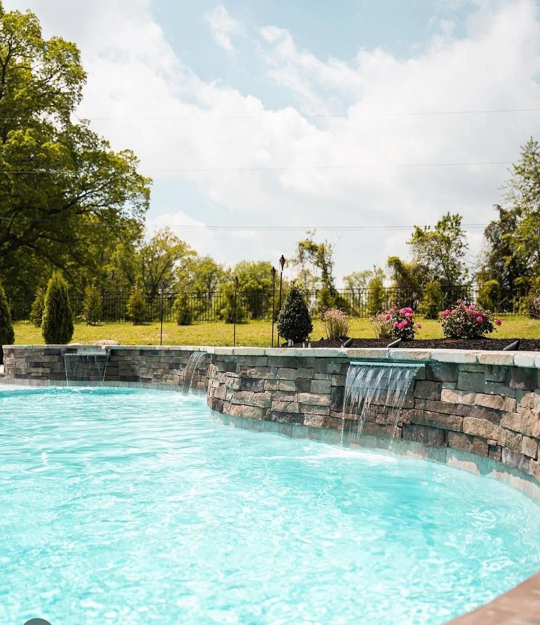 A wooden bench is sitting in front of a green hedge.