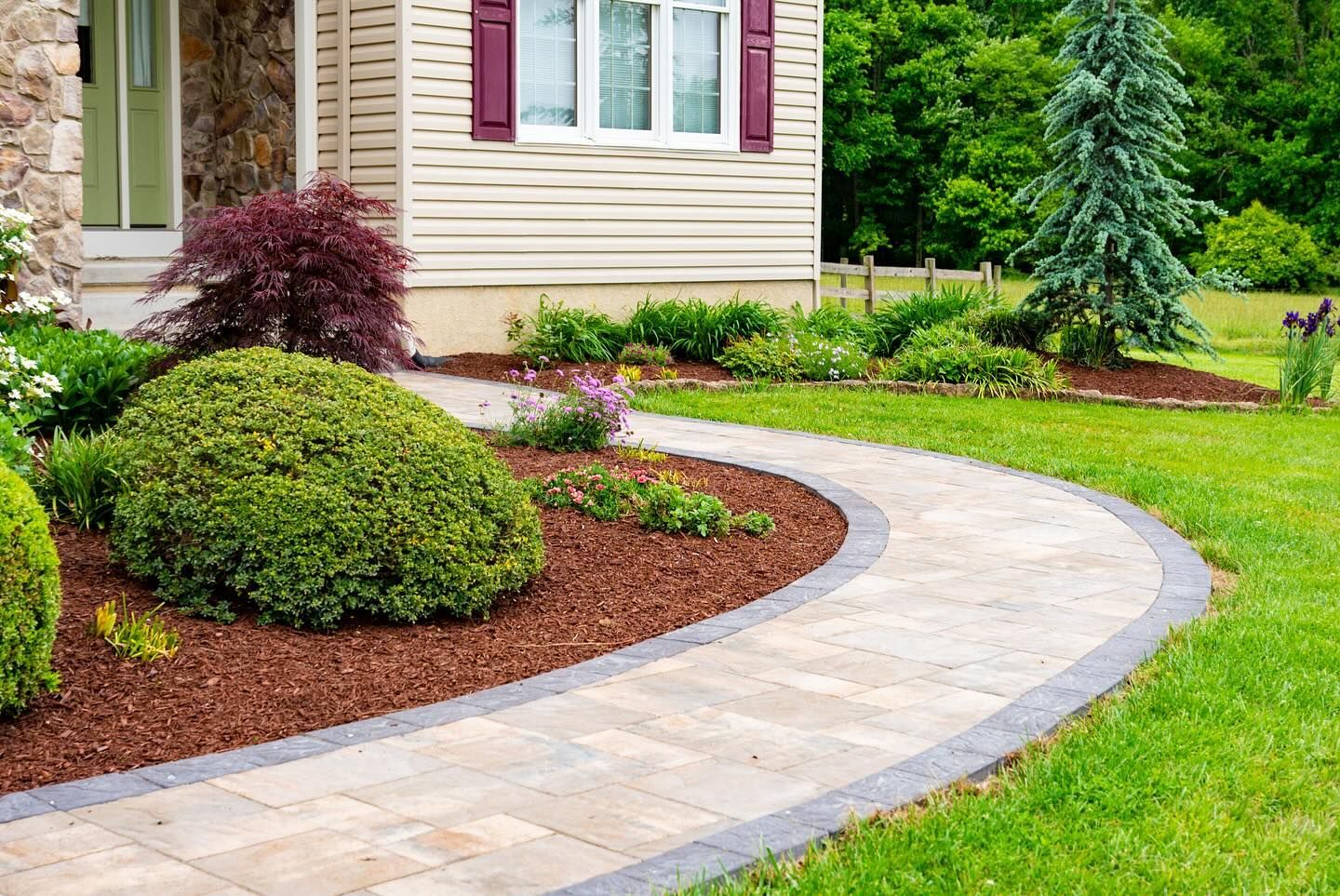 A brick walkway leading to a house in a lush green yard.