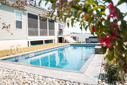 A large swimming pool in front of a house with a screened in porch.