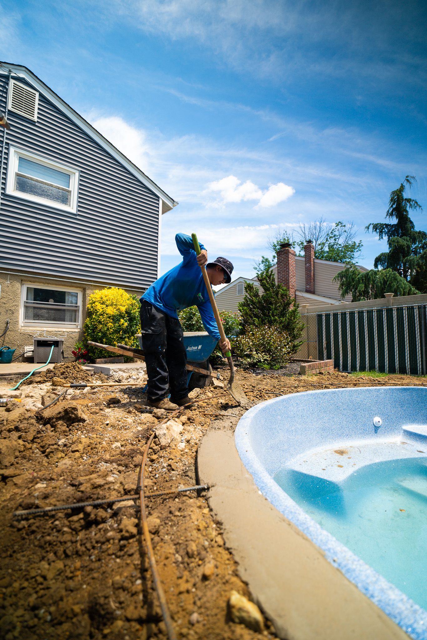 A man is digging in the dirt next to a swimming pool.