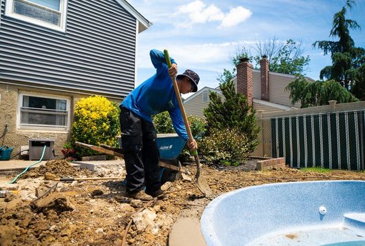 A man is digging in the dirt next to a pool.