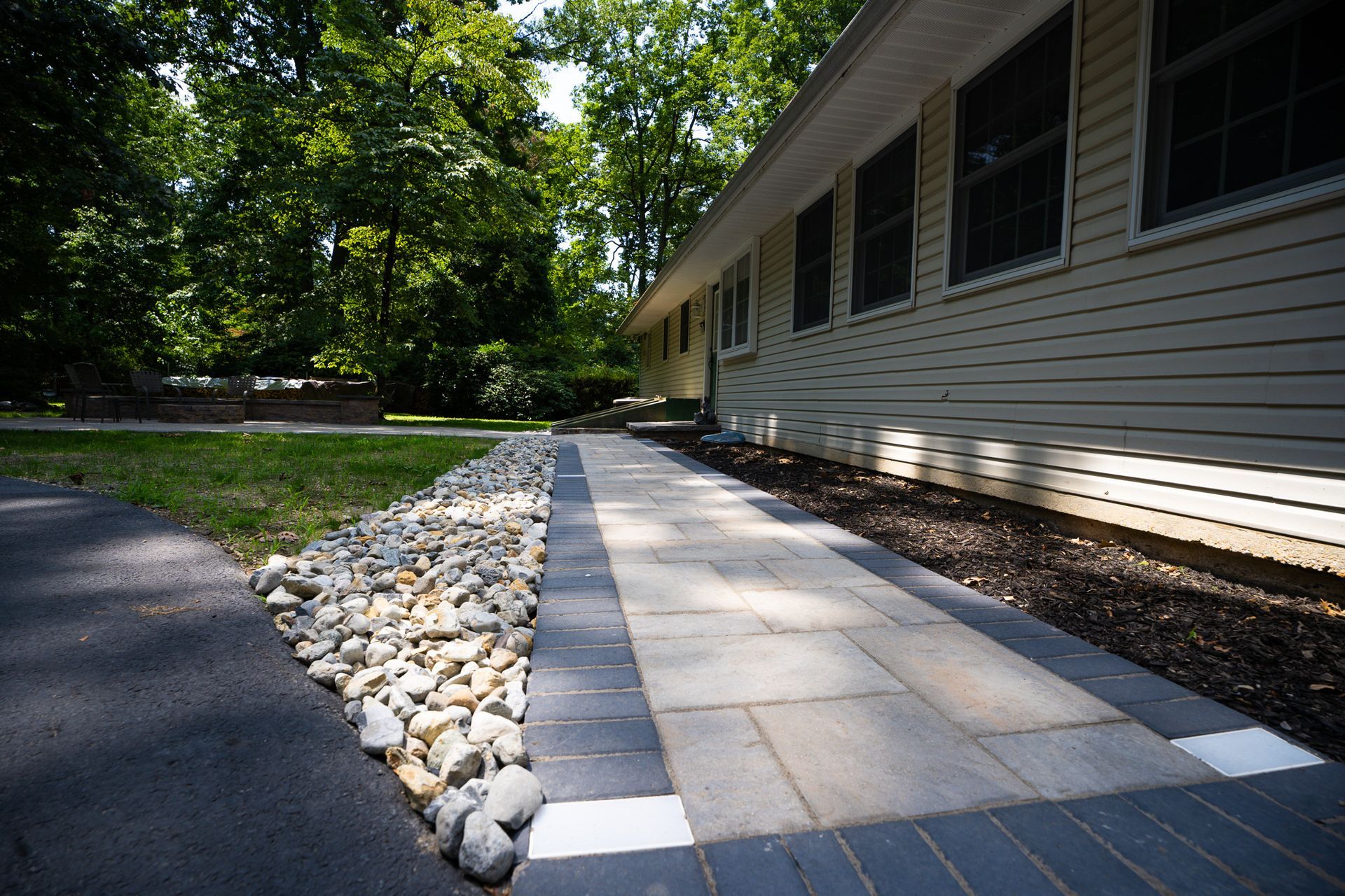 A stone walkway leading to a house with trees in the background