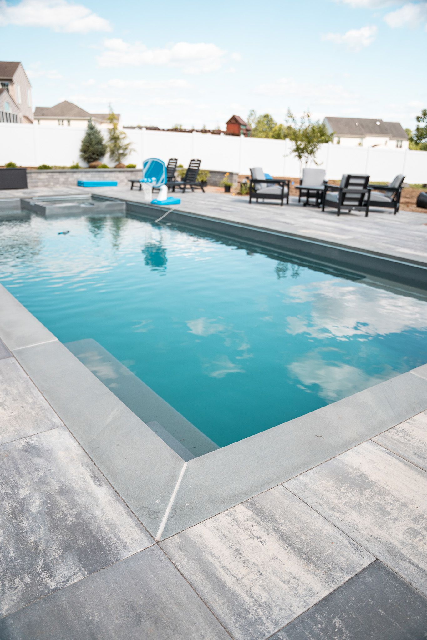 A large swimming pool surrounded by patio furniture and chairs in a backyard.