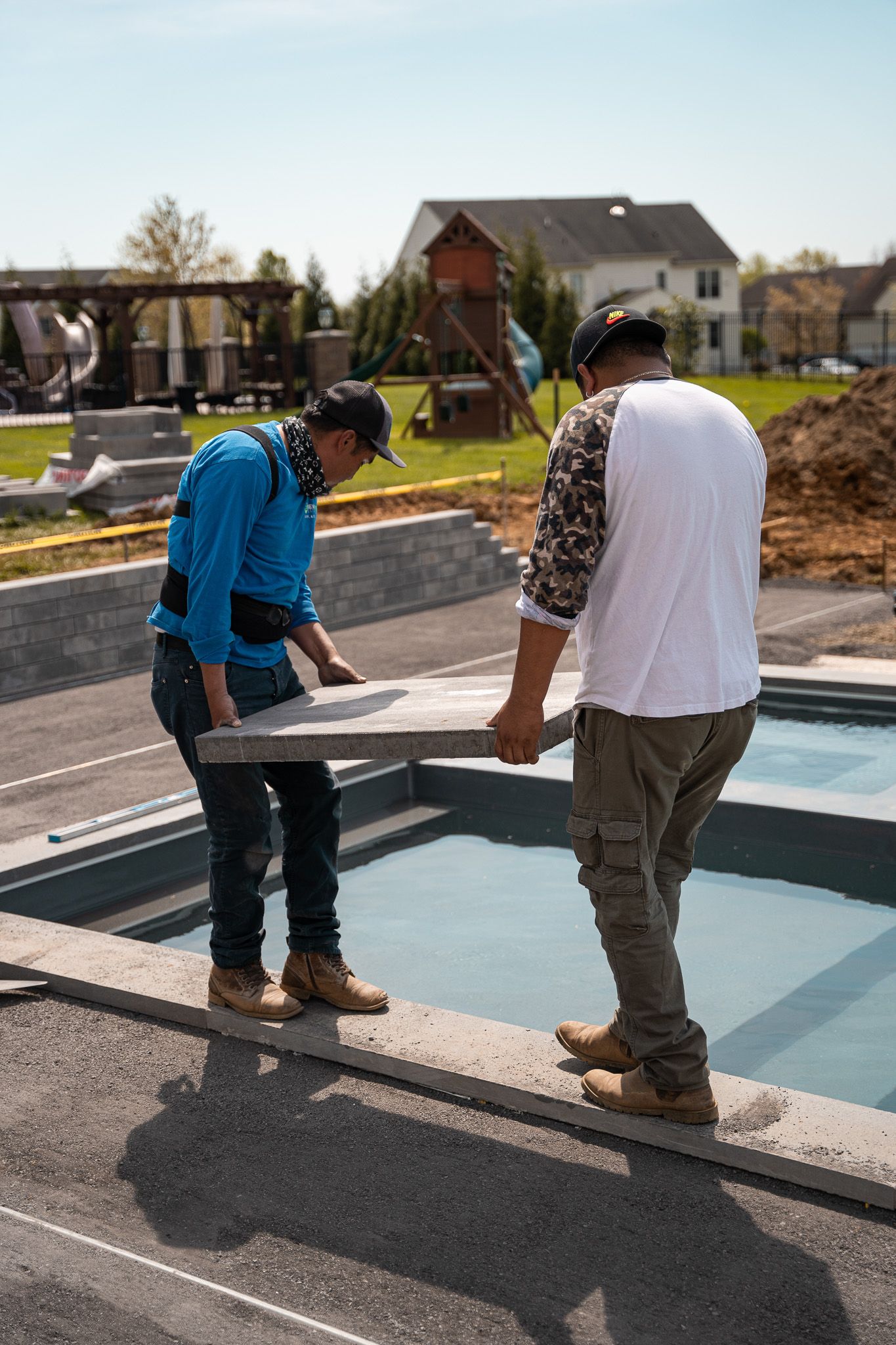 Two men are carrying a concrete slab into a pool.