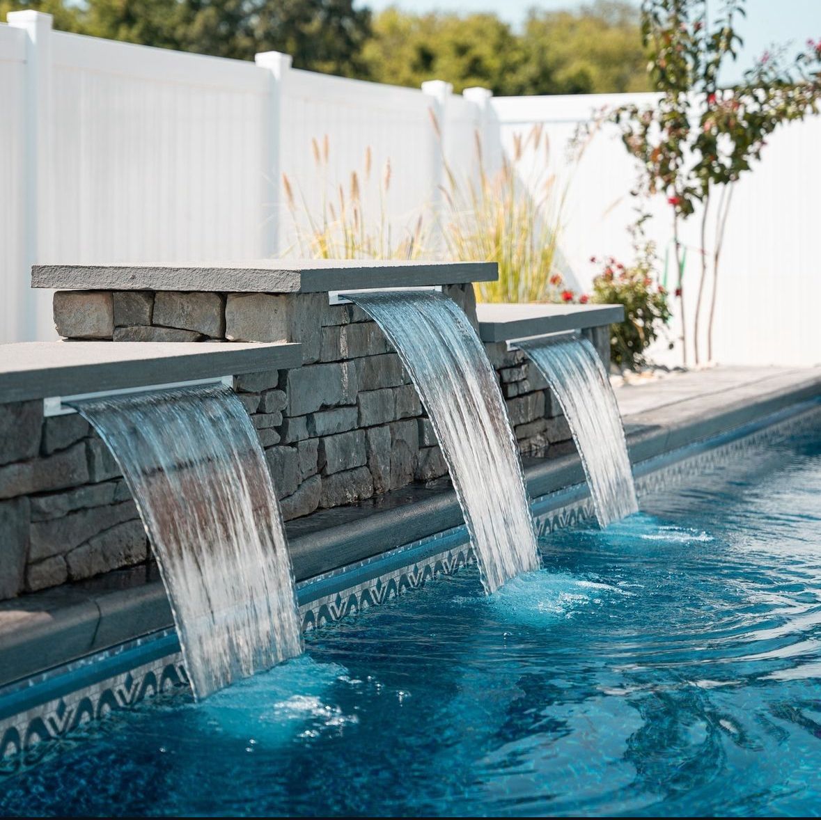 A waterfall in a swimming pool with a white fence in the background