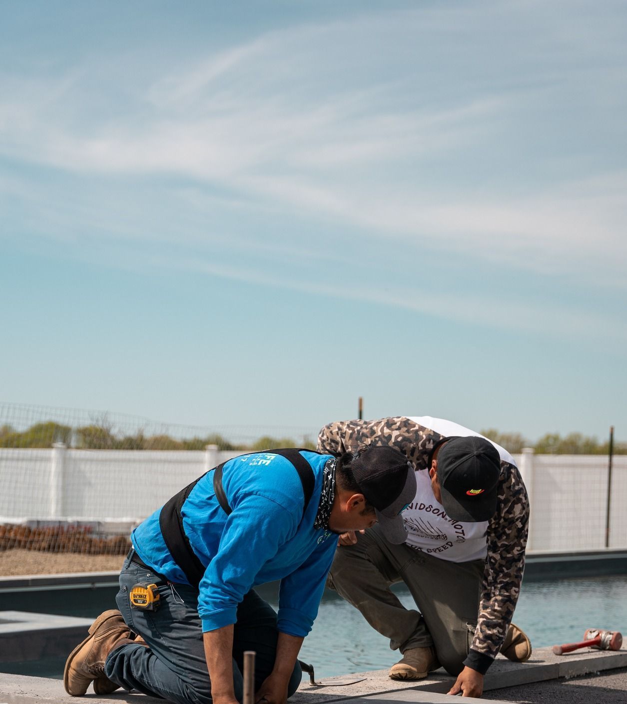 Two men are working on a swimming pool on a sunny day.