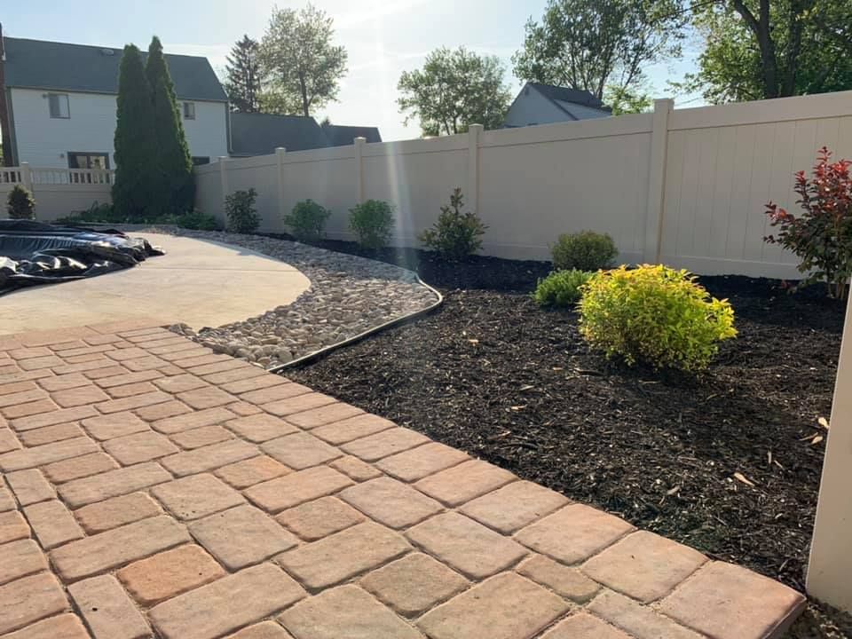 A brick walkway with a white fence in the background