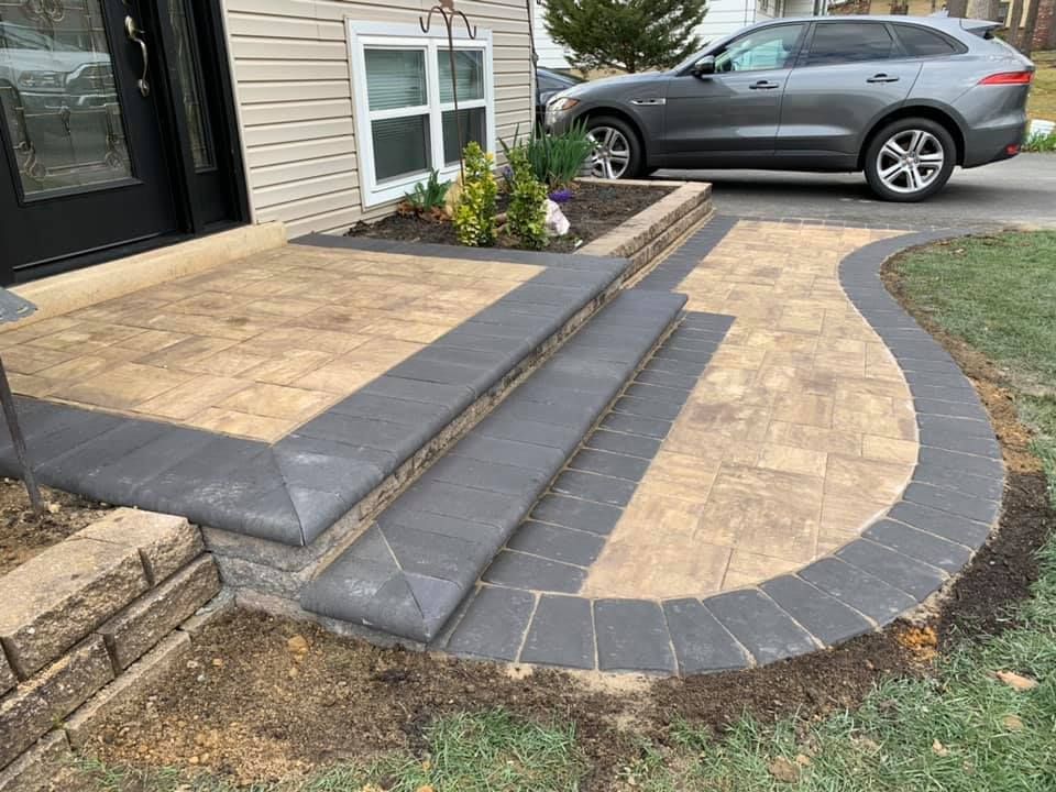 A car is parked in front of a house next to a brick walkway.