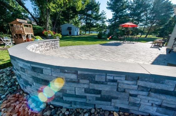 A brick wall surrounds a patio with a wooden playhouse in the background.