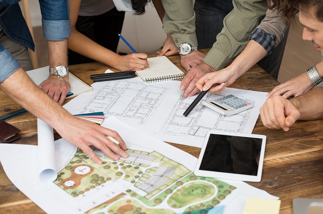 A group of people are sitting around a table looking at drawings.