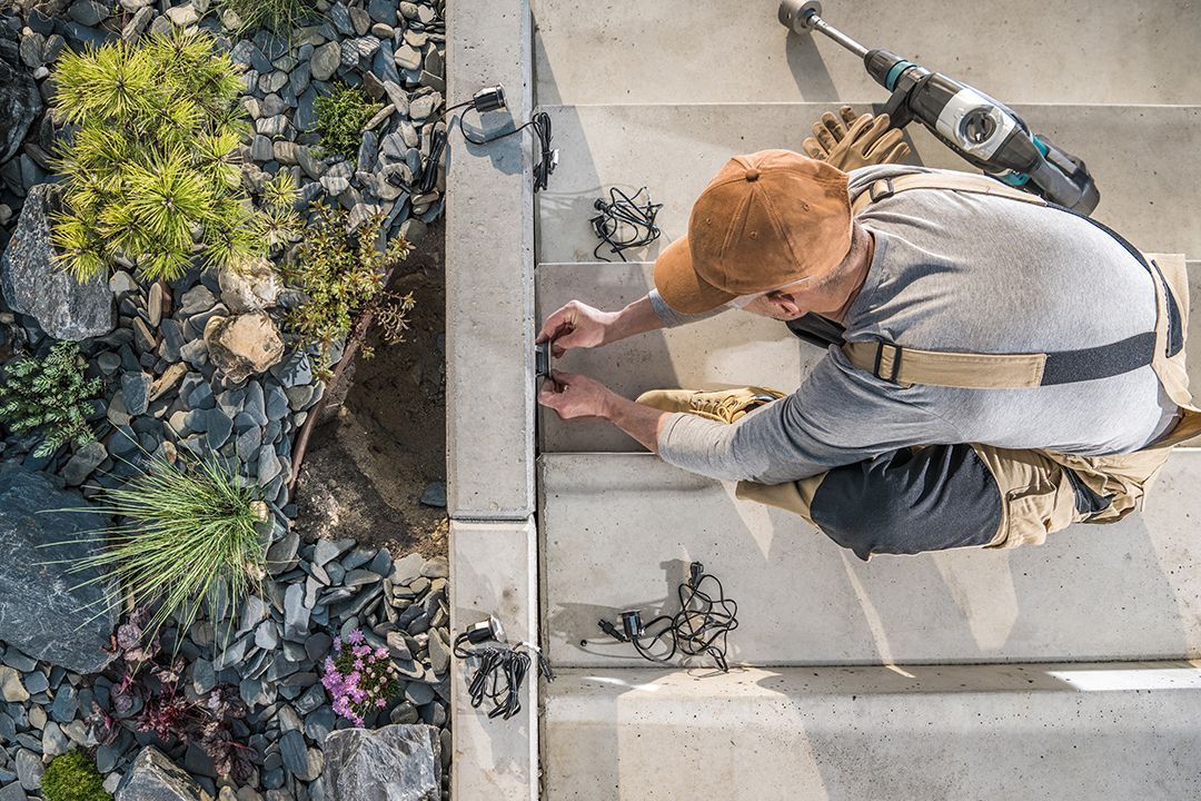 A man is kneeling down on the ground working on a concrete wall.