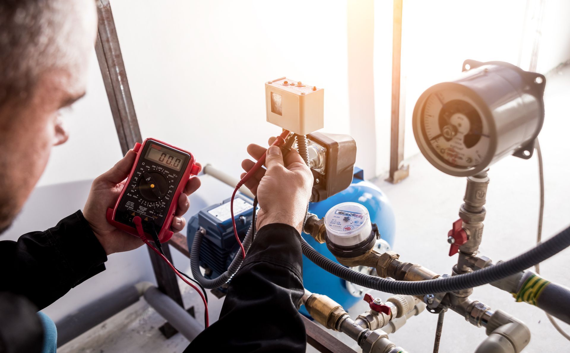 Person in blue shirt holding HVAC gauges with red, yellow, and black hoses.