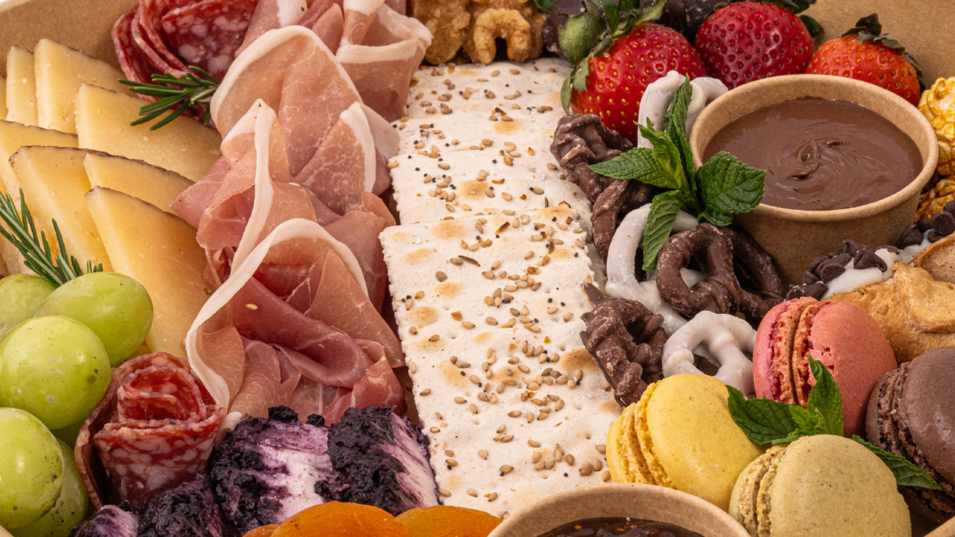 A variety of meats , cheeses , fruits and vegetables on a cutting board.