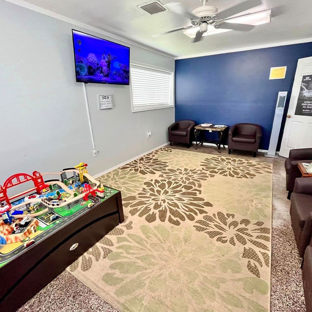 A living room with a train table , chairs , a television and a ceiling fan.