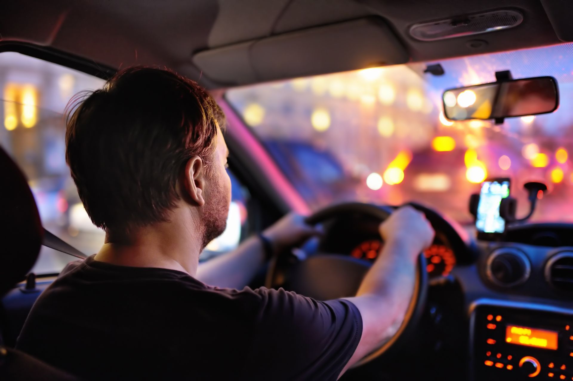 A man is driving a car at night with a cell phone on the dashboard.