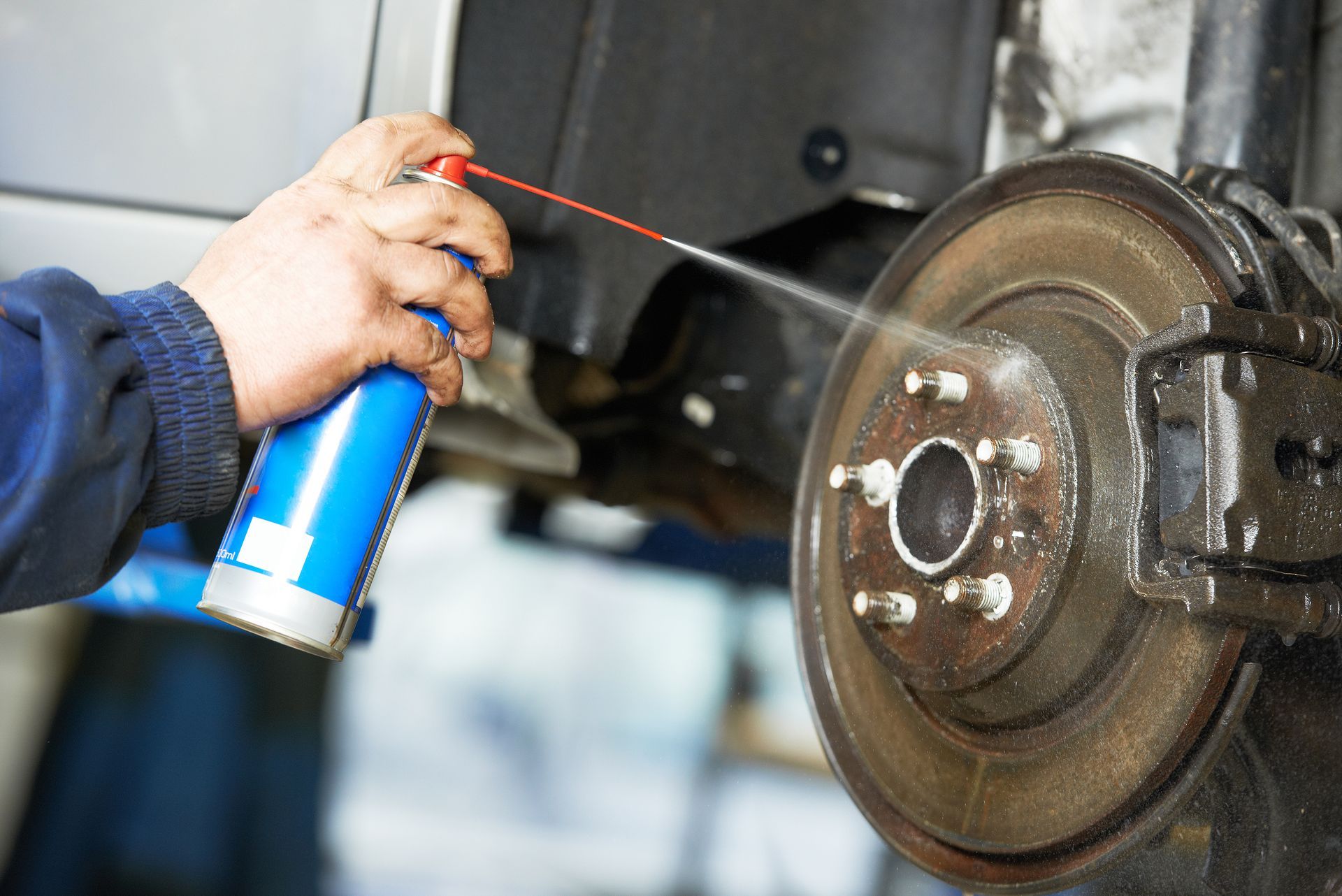 A person is spraying a can of lubricant on a brake disc.