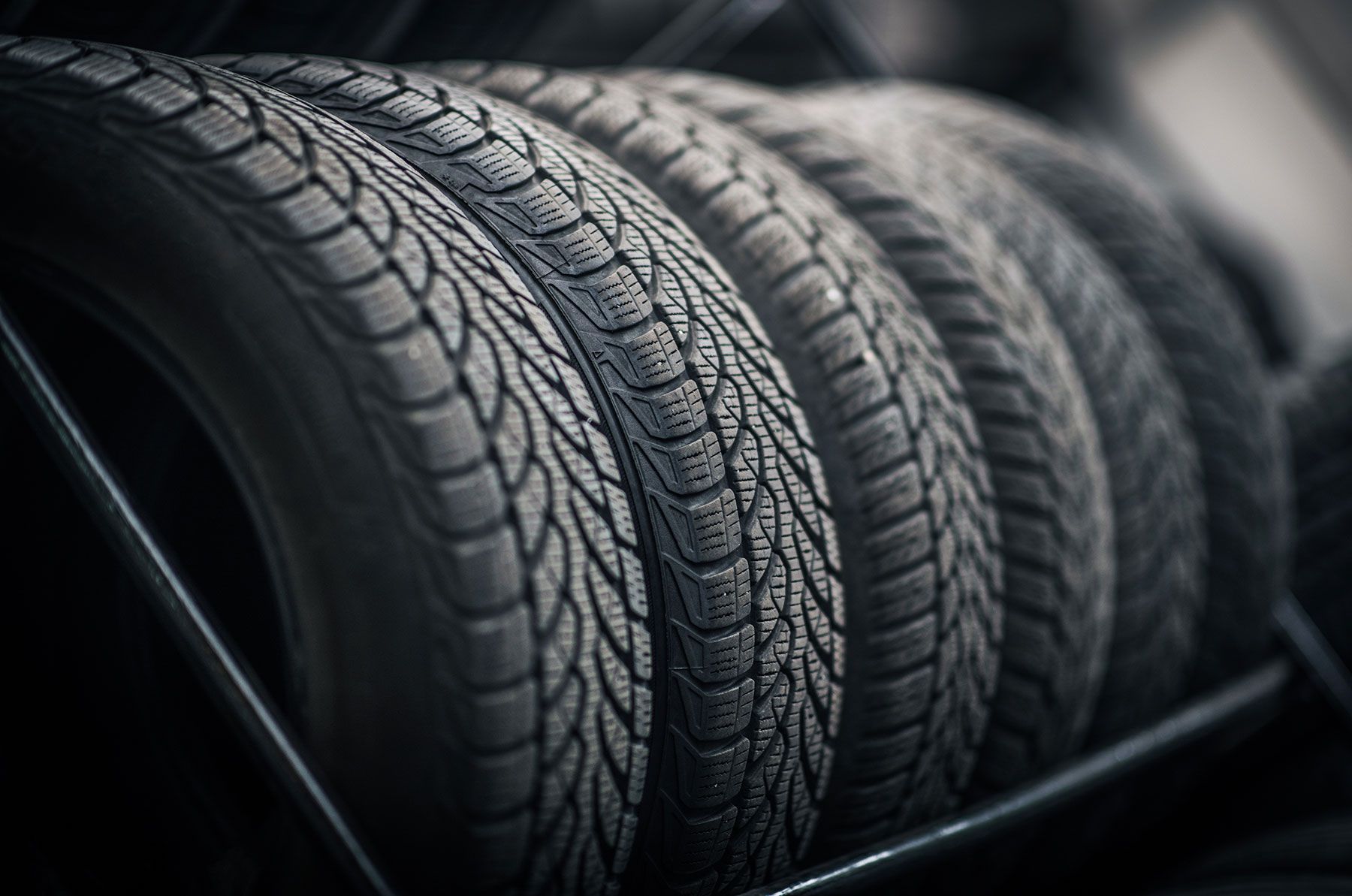 Row of black car tires with detailed tread patterns, stacked on a rack.