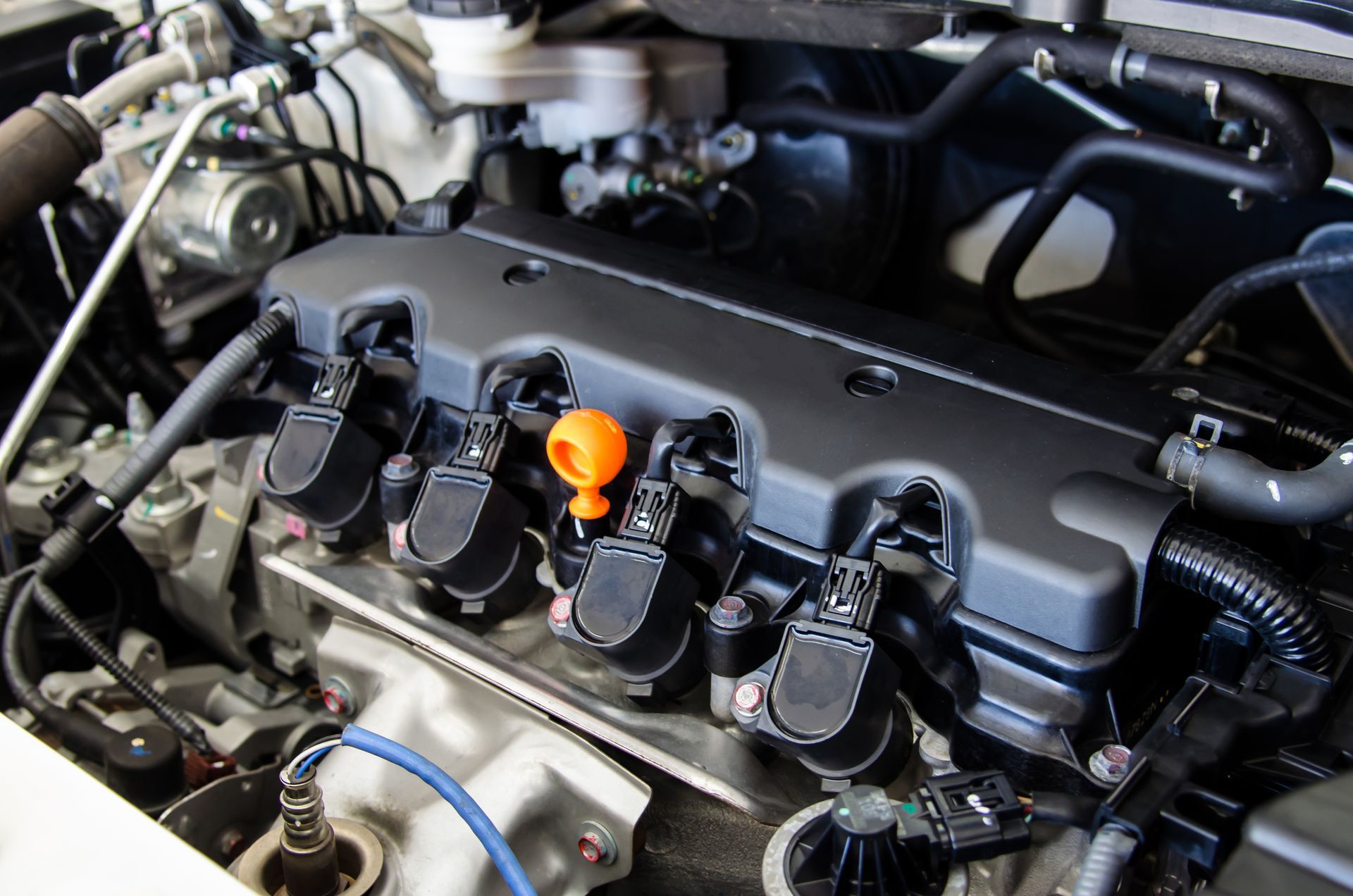 Car engine bay with a black valve cover and orange oil dipstick handle