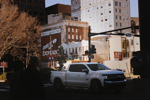 White truck driving at a city intersection with buildings and a faded Zatarain's advertisement.