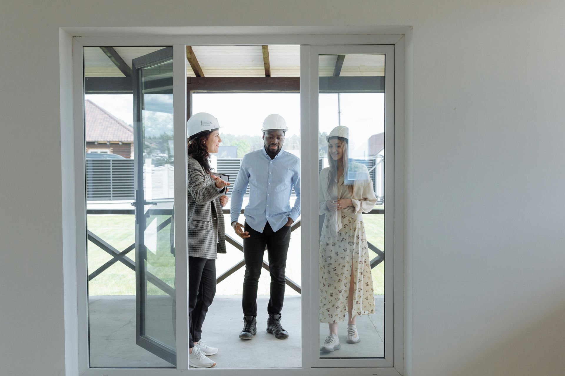 Three DOD contractors in hard hats stand in doorway, looking at a building's exterior.