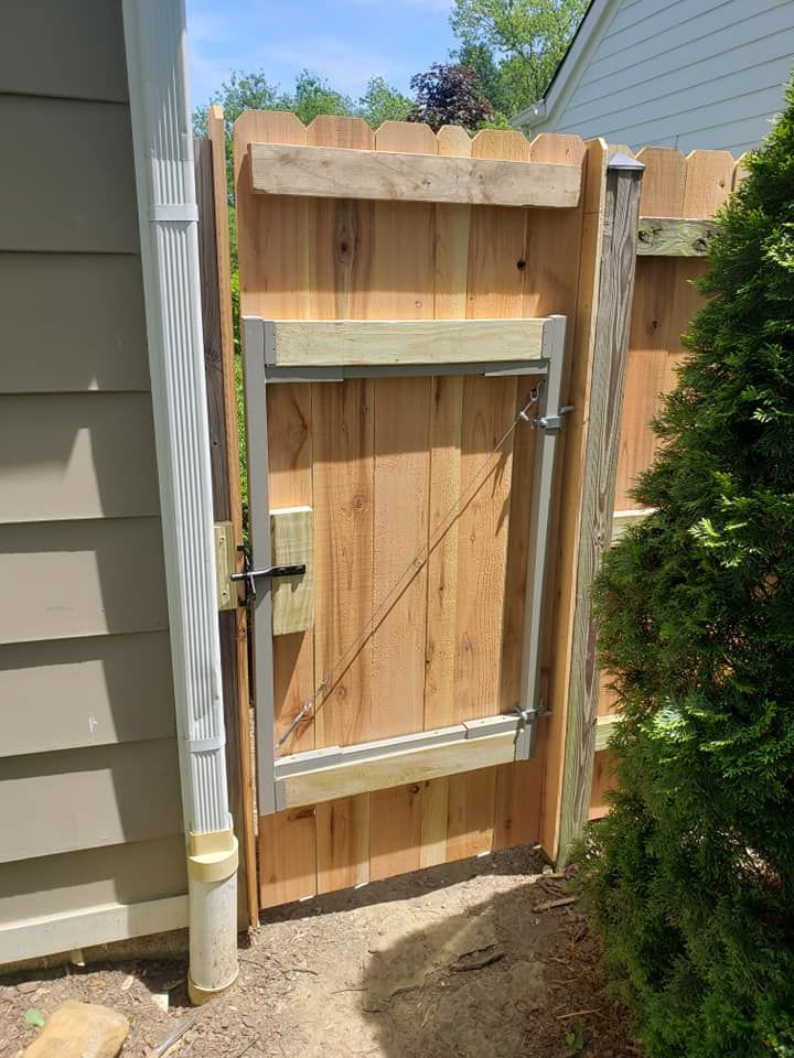A wooden gate is attached to a wooden fence next to a house.