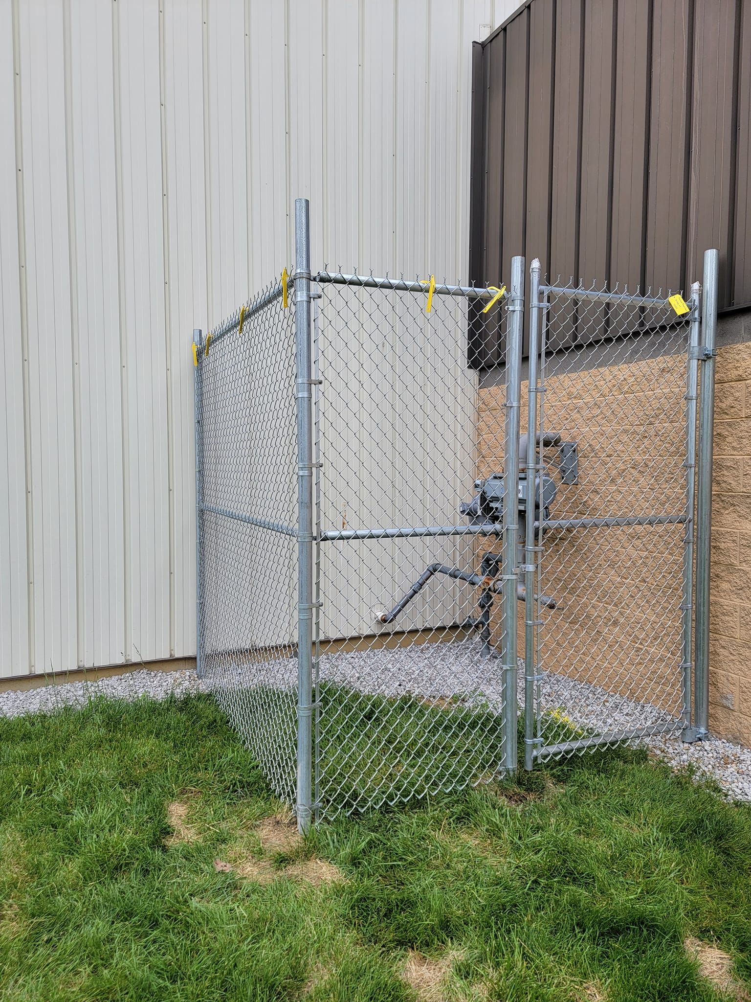 A chain link fence is sitting in the grass next to a building.