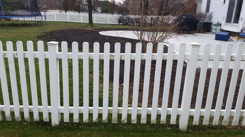 A white picket fence is sitting in the grass in front of a house.